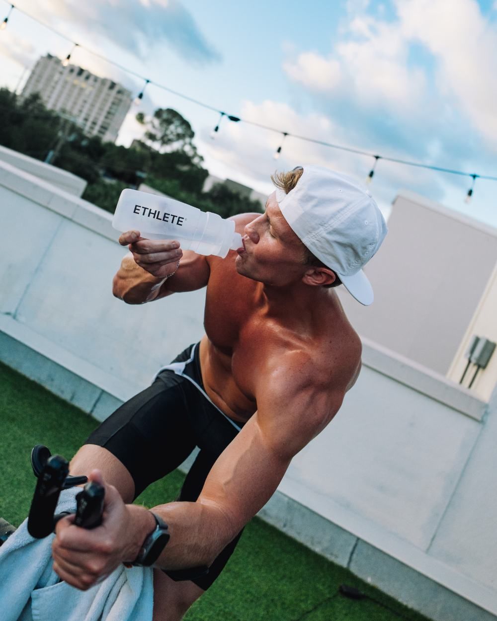 An athlete on a rooftop bike drinking from an ETHLETE bottle