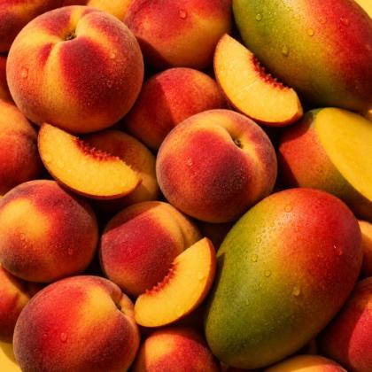 Ripe peaches and mangoes packed close, several sliced open