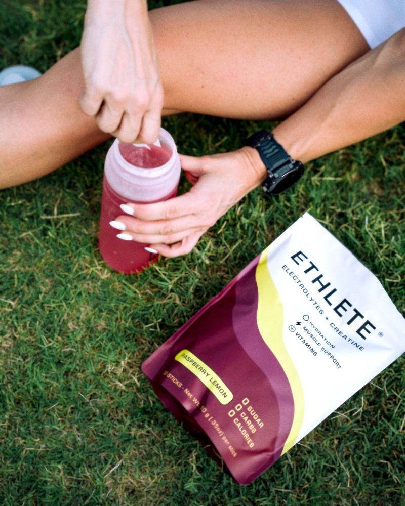 Hands stirring a mixed Raspberry Lemon drink in a bottle on the grass beside the pouch